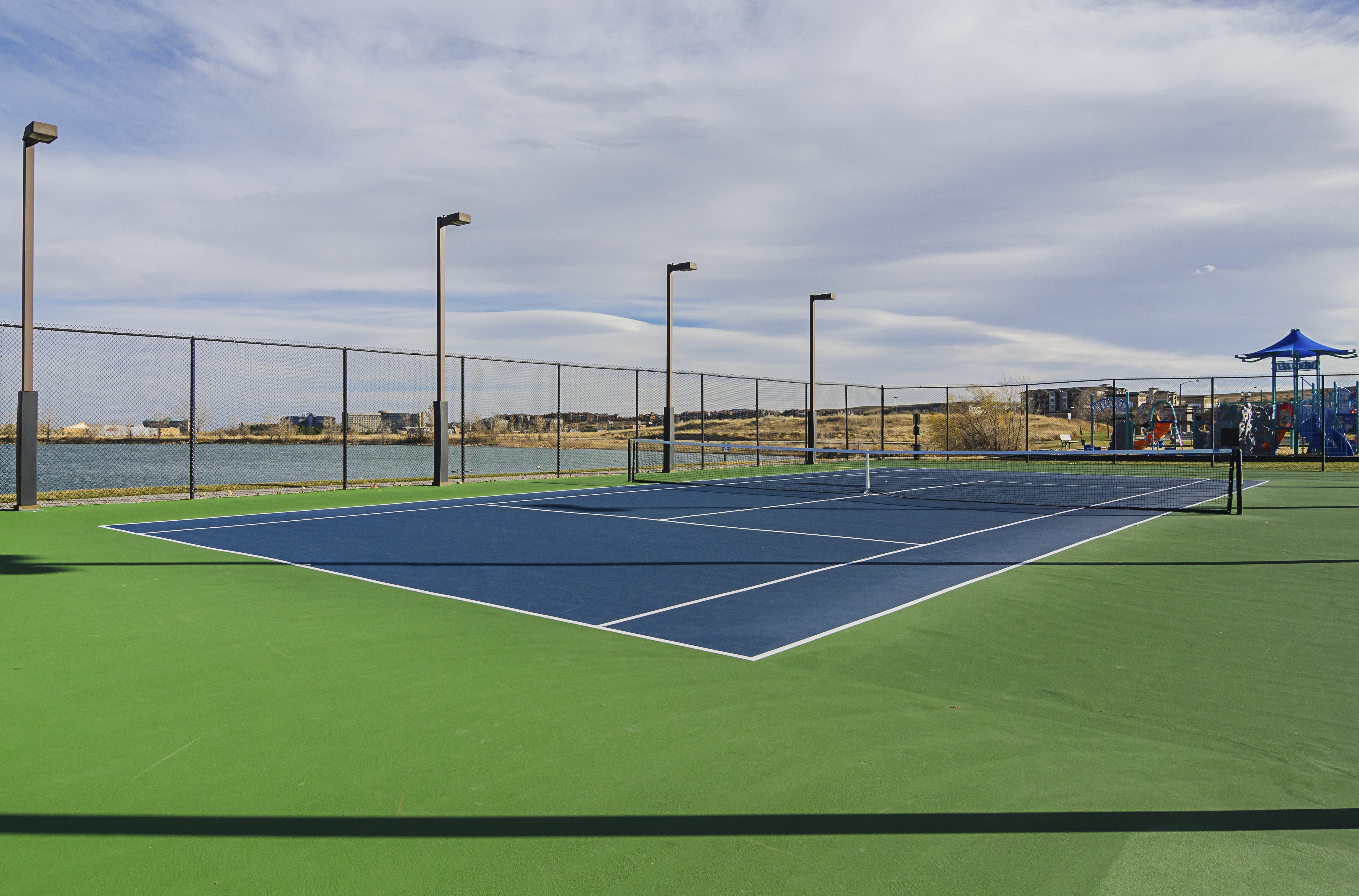 A tennis court with a blue sky and clouds in the background.